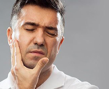 Photo of man in pain and holding the side of his face and needing an emergency dentist.