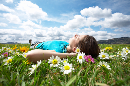 Young woman relaxing in a meadow of daisies with a blue sky and puffy clouds above her; for a representation of sedation dentistry from Sugar Land dentist Siny Thomas, DMD.