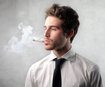 Young man wearing a shirt and tie and smoking; for information on tobacco use and dental implants.