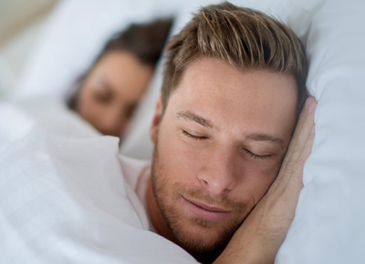 Man and woman sleeping on pillows in bed; for information on sleep apnea.