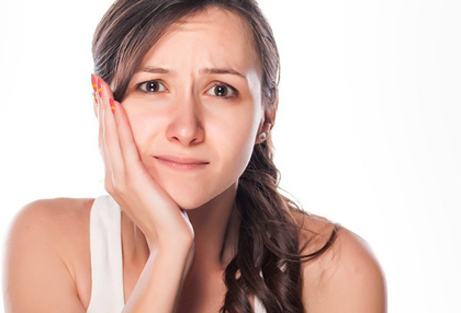 Young woman in white t-shirt holding the right side of her face due to TMJ/TMD pain.