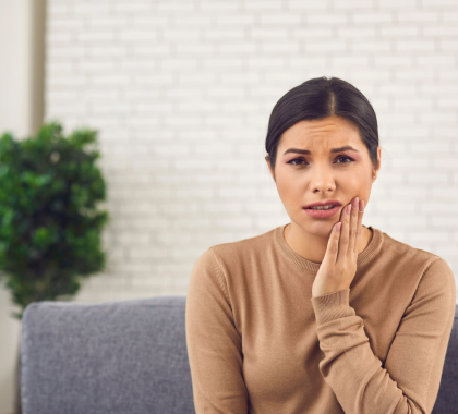 Brunette woman holding the left side of her face, portraying concern of a brown wisdom tooth.